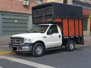 Camioneta de carga con mercadería asegurada en la caja, frente a un edificio.